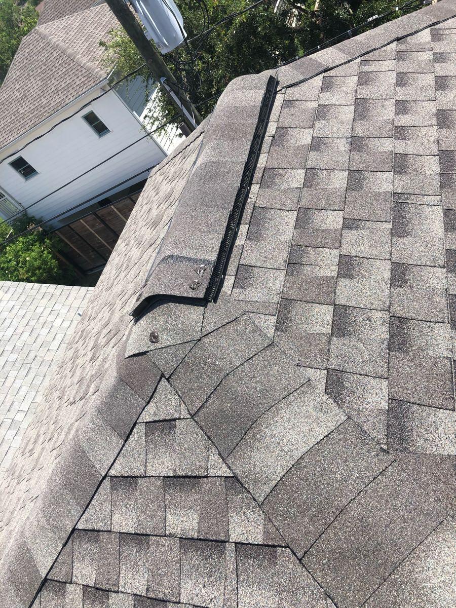 Close view of gray roof shingles and a ridge vent at a roof intersection