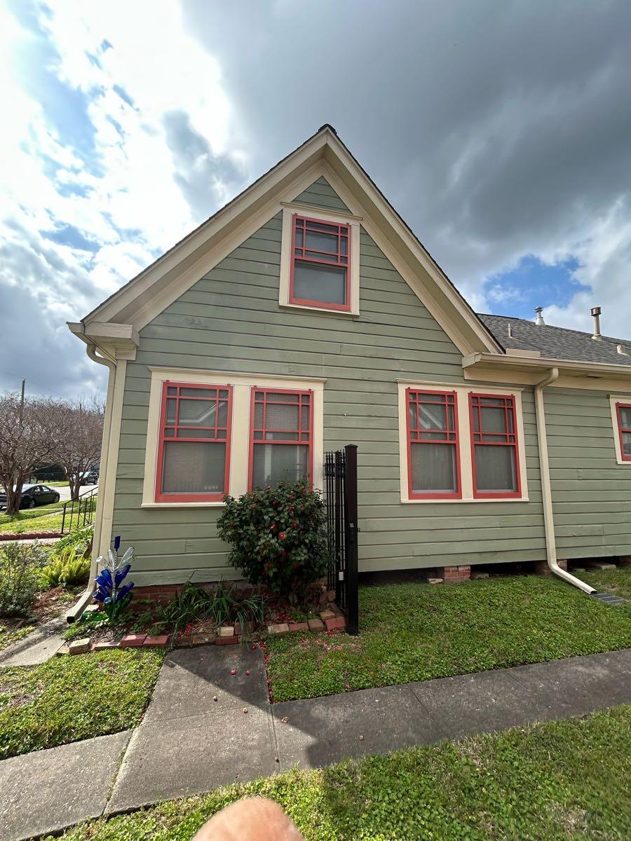 Side elevation of a green Woodland Heights home with lap siding, white trim, and coral window frames